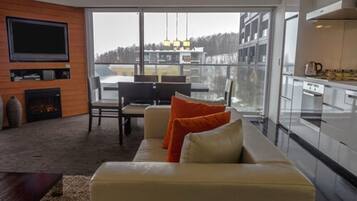 A modern living room with a sofa, television, fireplace, and large windows overlooking a cityscape.