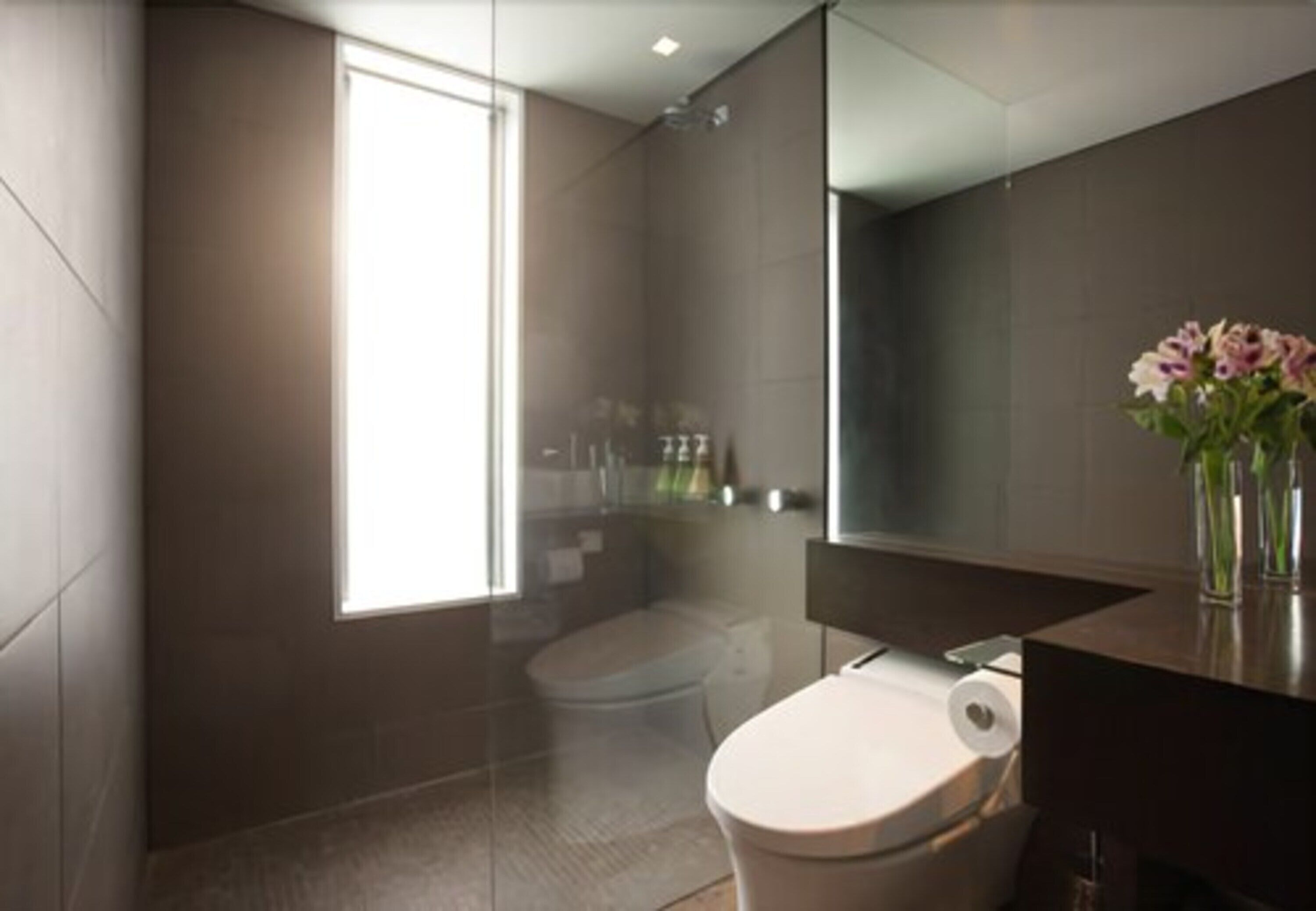 A modern bathroom with a toilet, a shower, and a large mirror above the sink.
