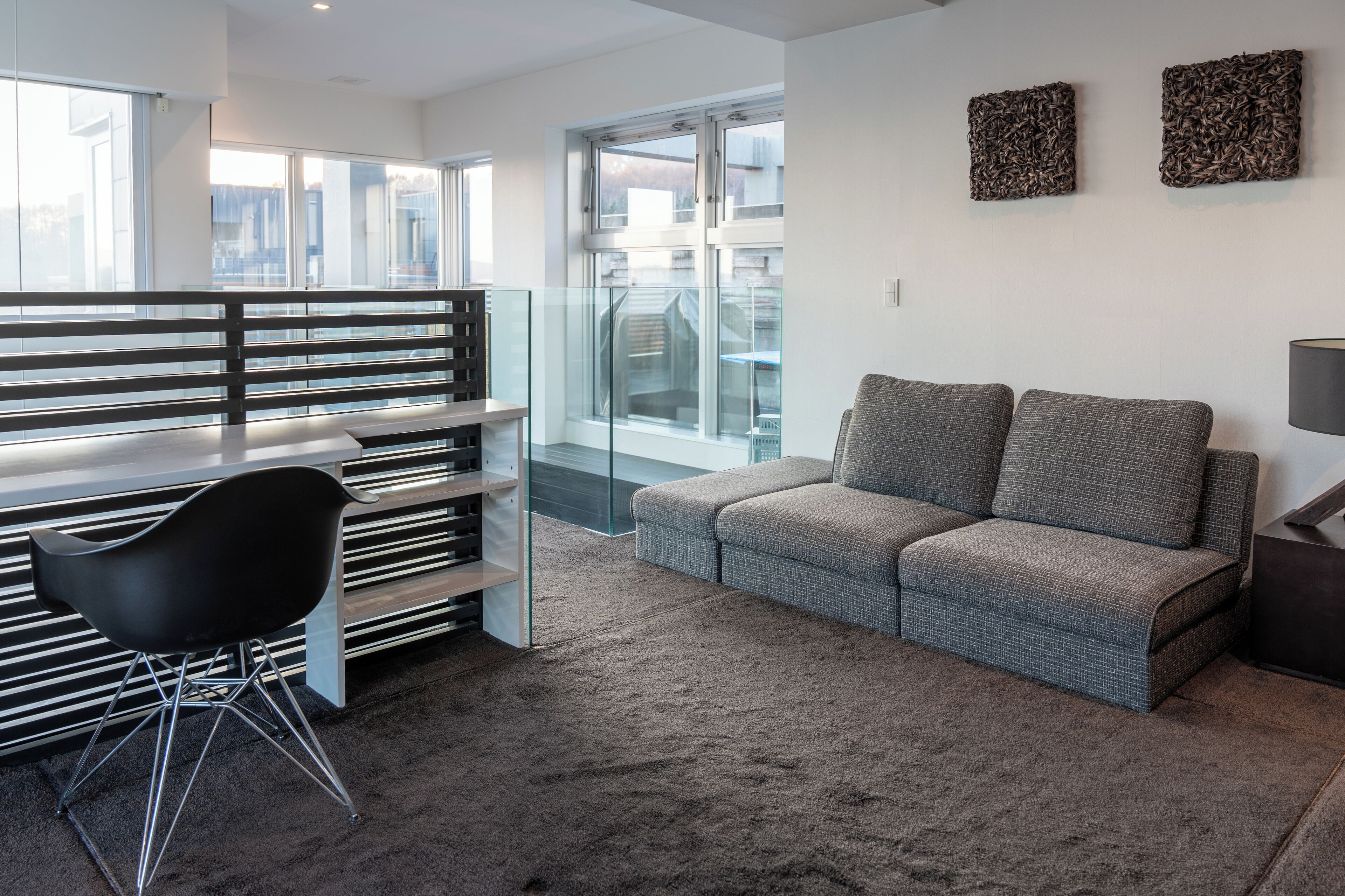 A modern living area with a sofa, a black chair, and a glass partition.