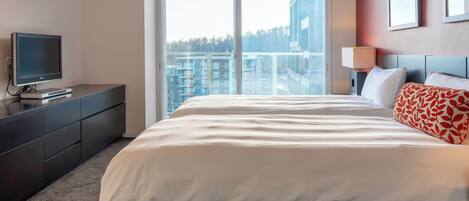 A hotel room with a large bed, a flat-screen TV, a dresser, and a window with a city view.
