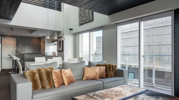 Una sala de estar moderna con un sofá gris, una mesa de centro y una cocina al fondo.