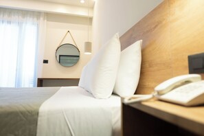 A hotel room with a bed, a bedside table with a phone, a round mirror, and a hanging light fixture. - Malia Holidays Hotel (Hersonissos)