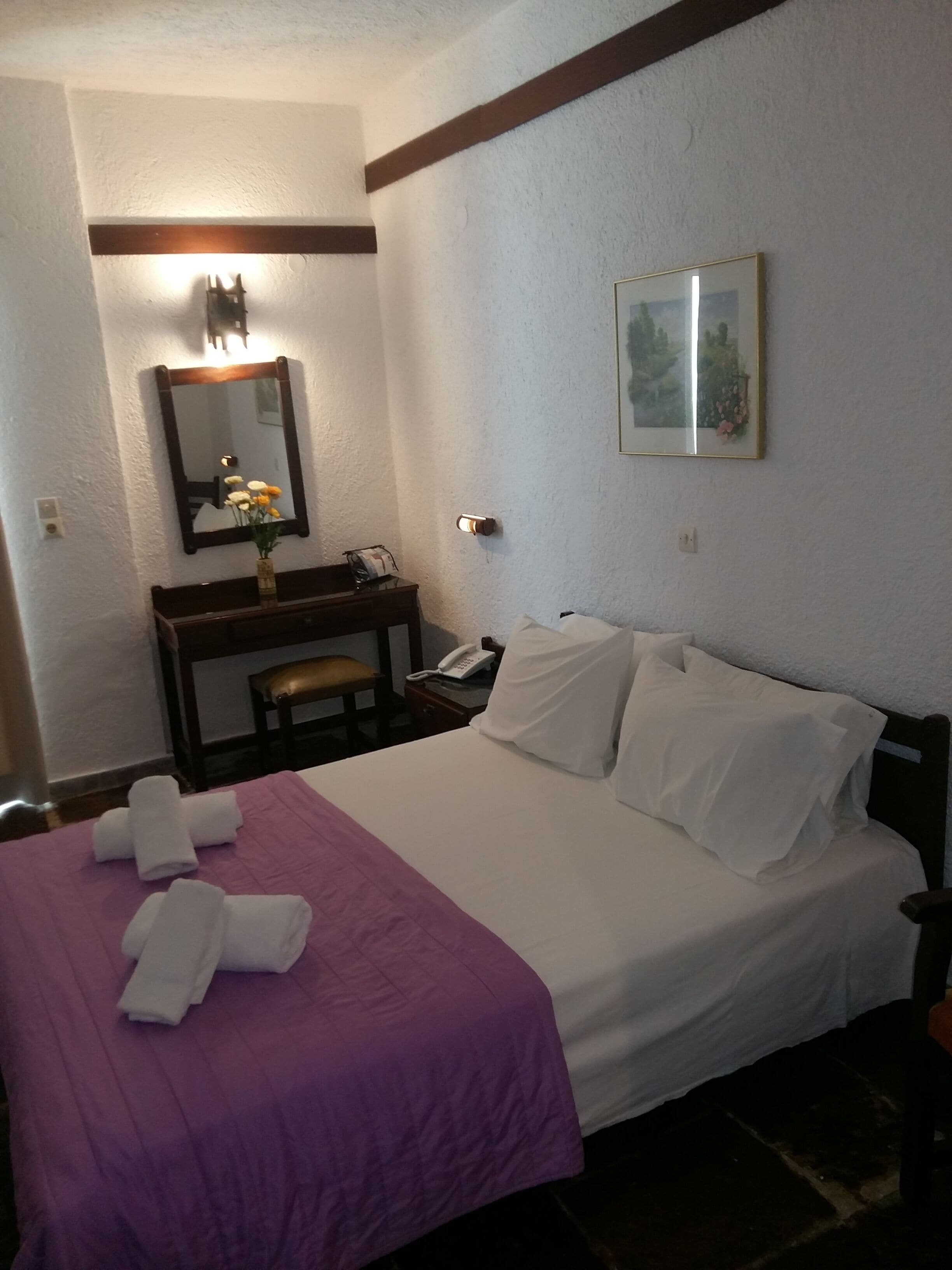 A hotel room with a bed, a desk with a telephone, a mirror, and a framed picture on the wall.