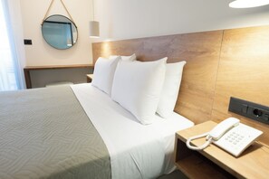 A hotel room with a neatly made bed, a bedside telephone, and a round mirror on the wall.