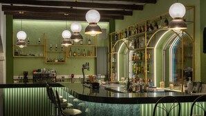 A bar area with a green wall, shelves with bottles, and bar stools.