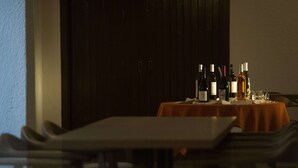A dining area with a table set for two, a dark wooden door in the background, and bottles of wine on the table.