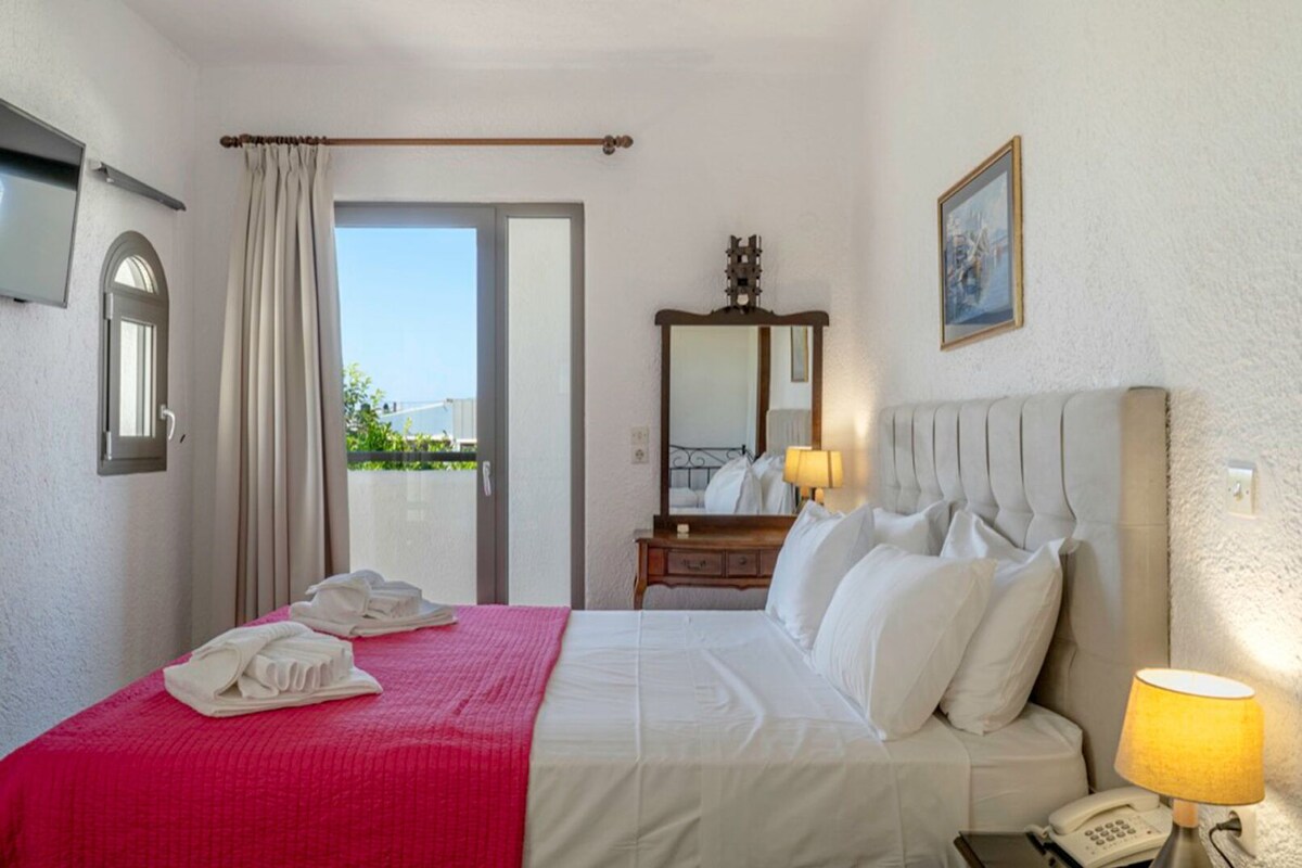 Une chambre d’hôtel avec un lit, une lampe de chevet, un téléphone, un miroir et une fenêtre avec des rideaux.