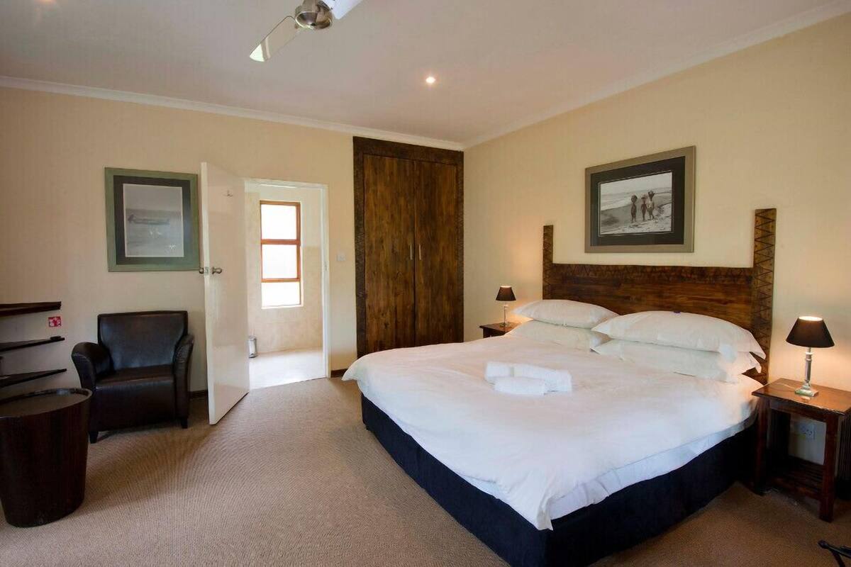A hotel room with a large bed, a wooden wardrobe, a desk with a chair, and a framed picture on the wall.