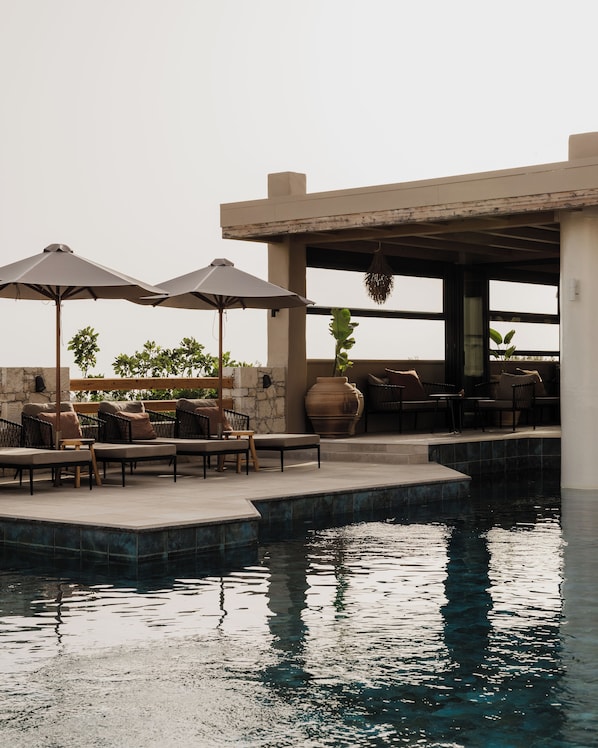 A rooftop pool area with lounge chairs, umbrellas, and a stone wall.