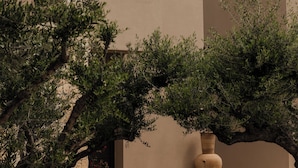 A person leaning on a balcony railing of a building with a beige facade and a small window. - Momi Slow Living Hotel (Hersonissos)