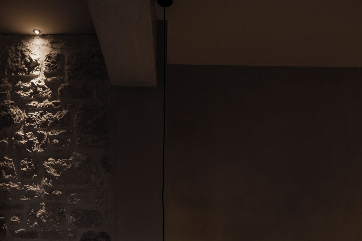 A bedroom with a stone wall, a bed with white bedding, and a hanging light fixture.