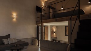 A modern loft-style living space with a mezzanine, a sofa, a coffee table, and a small kitchen area. - Momi Slow Living Hotel (Hersonissos)