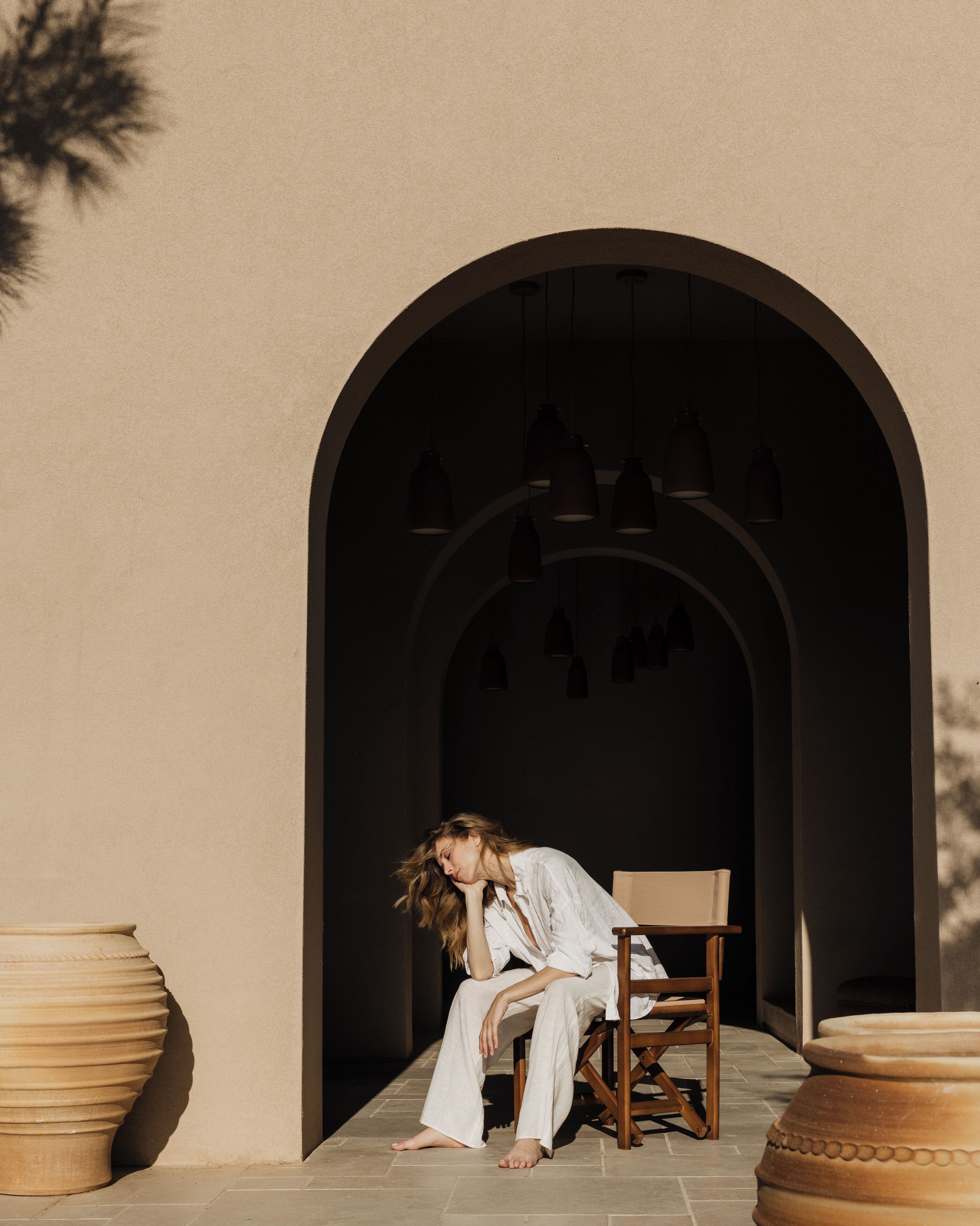 A person sitting on a chair in a doorway with a tiled floor, surrounded by large planters.