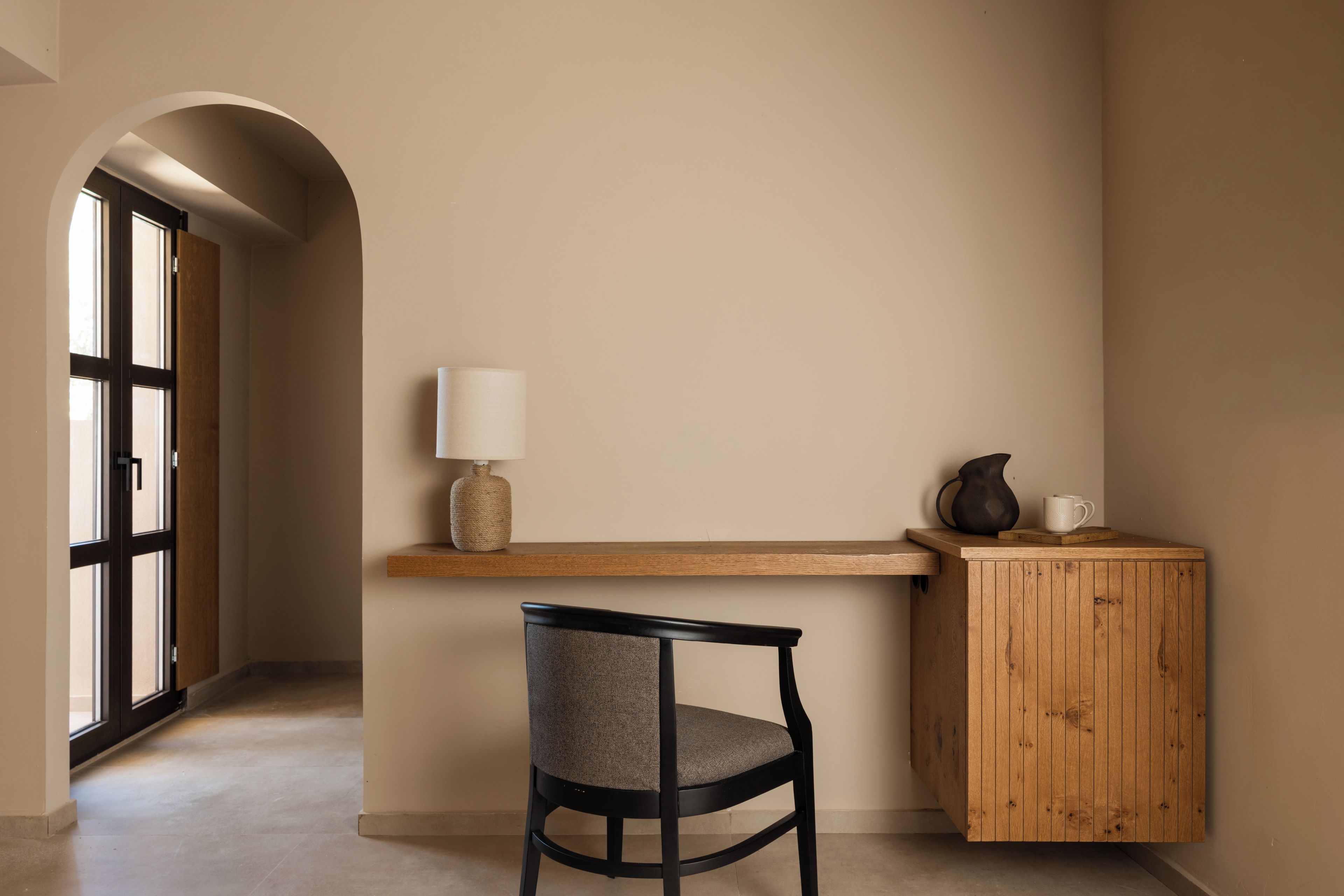 A minimalist room with a wooden desk, a chair, a lamp, and a cabinet.