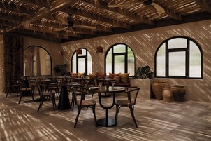 Un comedor espacioso con varias mesas y sillas, ventanas amplias y un diseño moderno en el techo.