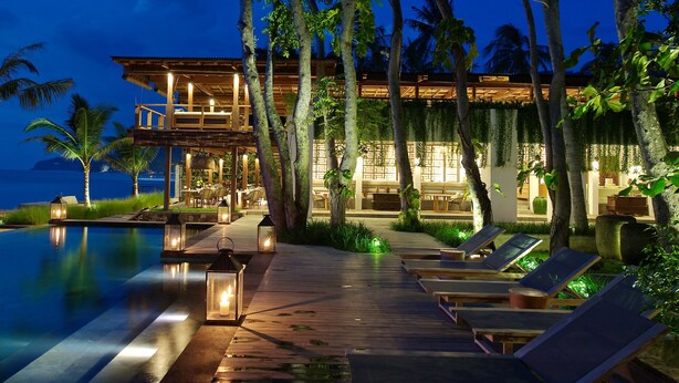 A resort with an infinity pool, lounge chairs, and a well-lit building with a view of the ocean. - Jeeva Santai Villas (Senggigi)