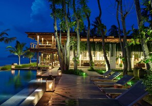 A resort with an infinity pool, lounge chairs, and a well-lit building with a view of the ocean. - Jeeva Santai Villas (Senggigi)