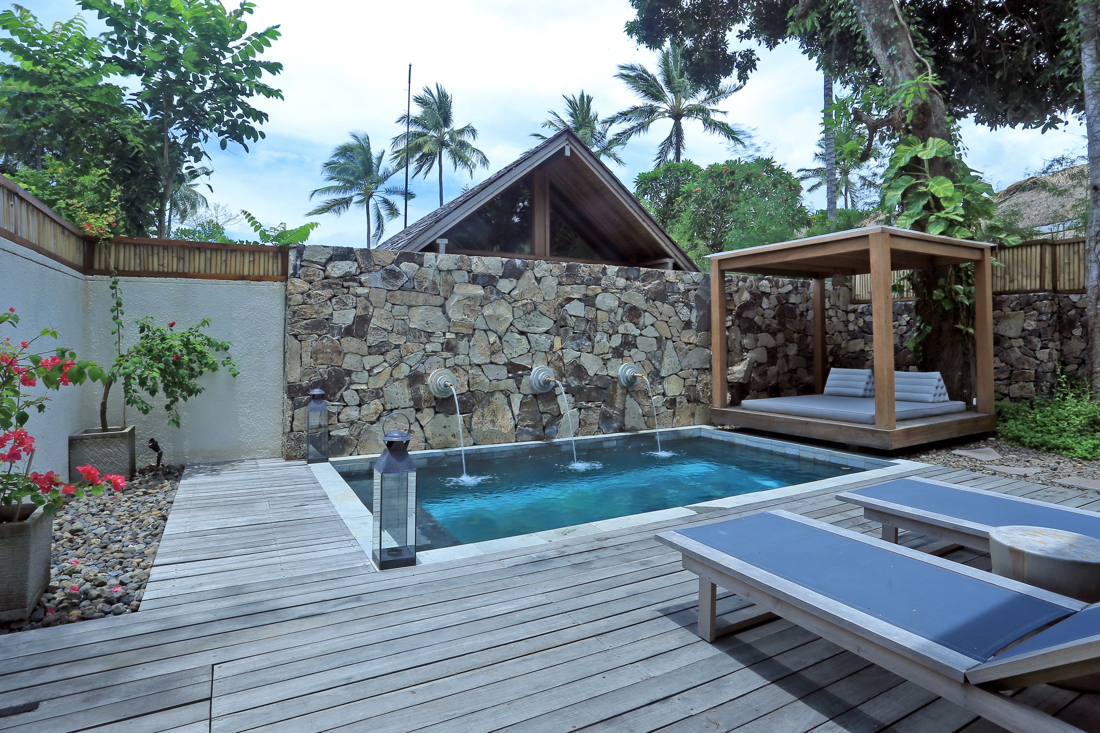 A wooden deck with a stone wall, a small pool with water features, and a wooden gazebo.