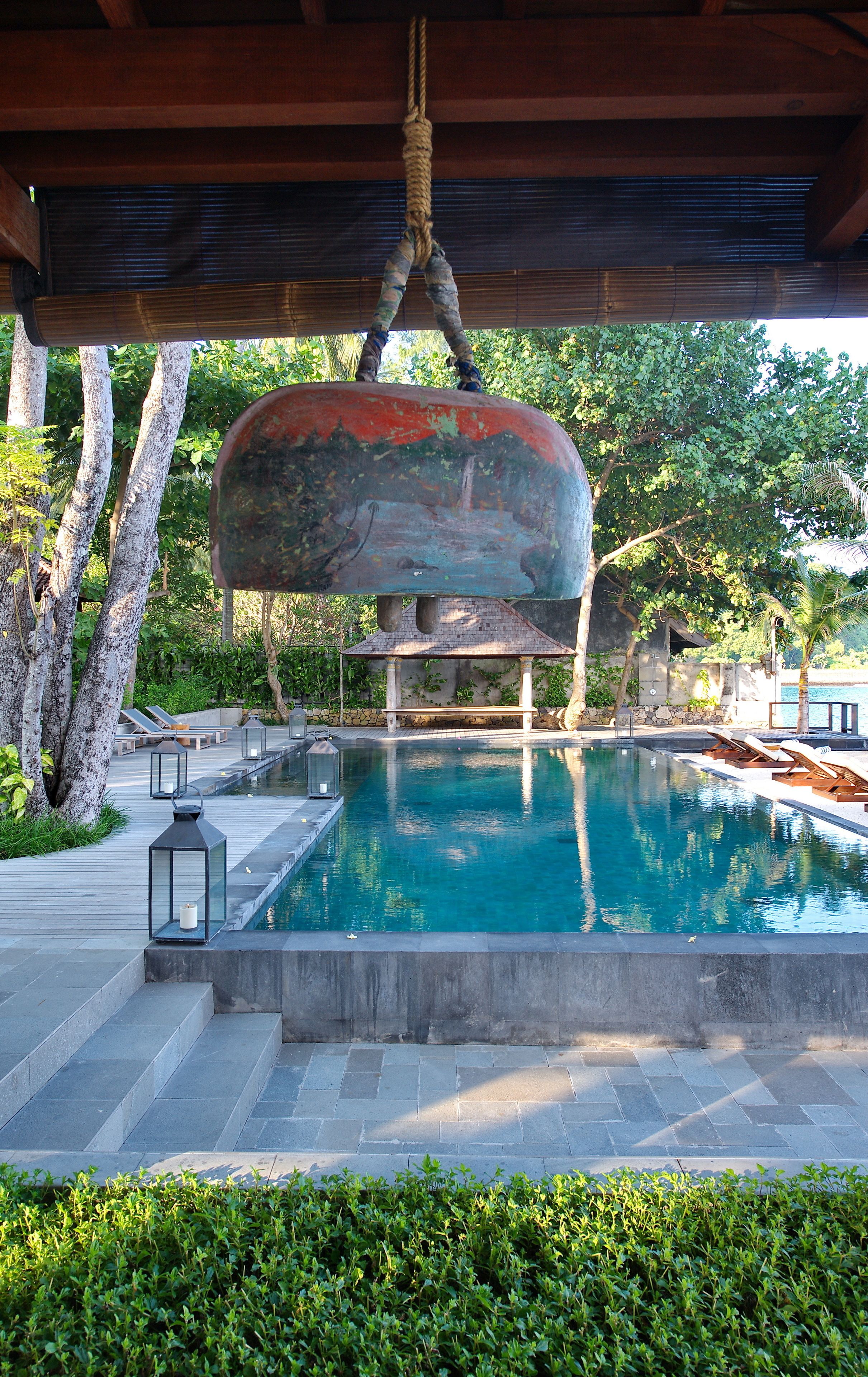 A pool area with a large, rustic water feature, lounge chairs, and a gazebo.
