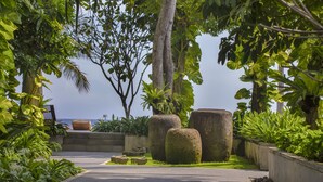 A pathway flanked by lush greenery and large stone planters, leading to a view of the sea. - Jeeva Santai Villas (Senggigi)