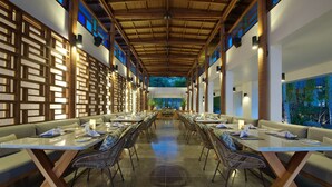 A spacious indoor dining area with long tables, cushioned seating, and a high ceiling with wooden beams. - Jeeva Santai Villas (Senggigi)