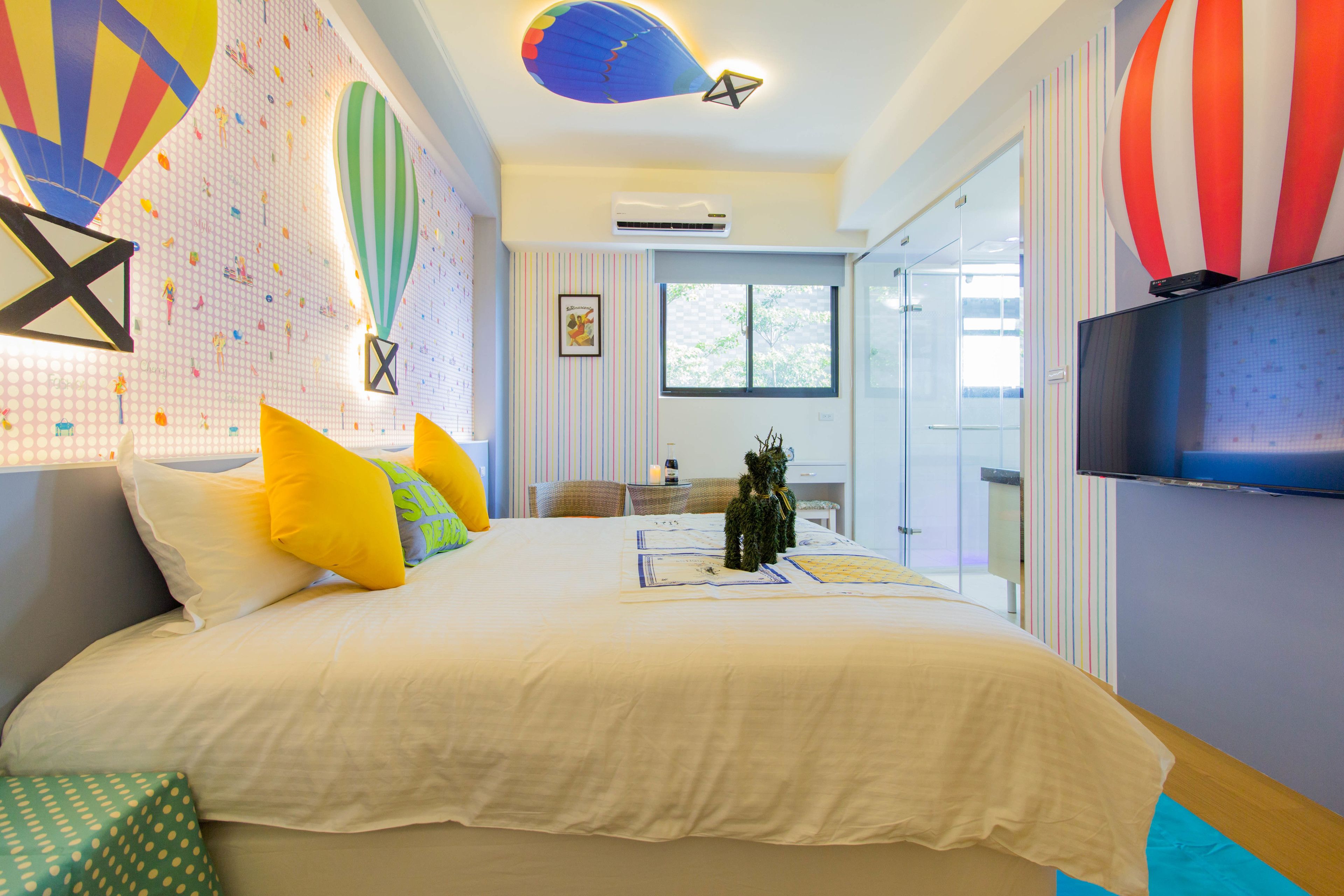 A modern hotel room with a large bed, colorful pillows, a television, and a view of the outdoors.