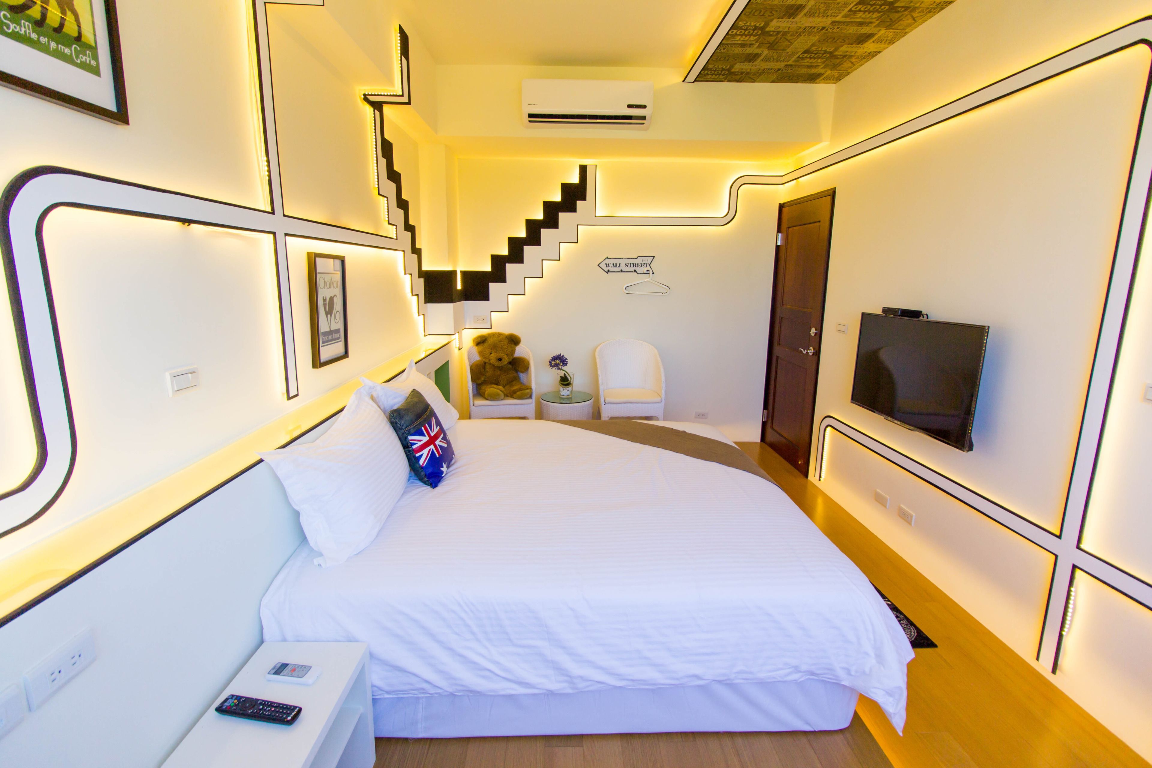 A hotel room with a bed, a TV, a teddy bear, a chair, and a staircase.