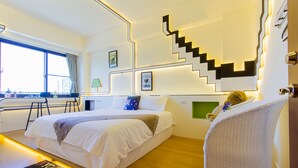 A modern hotel room with a large bed, a desk, a chair, a staircase, and a window with a view of buildings. - F One B&B (Wujie)