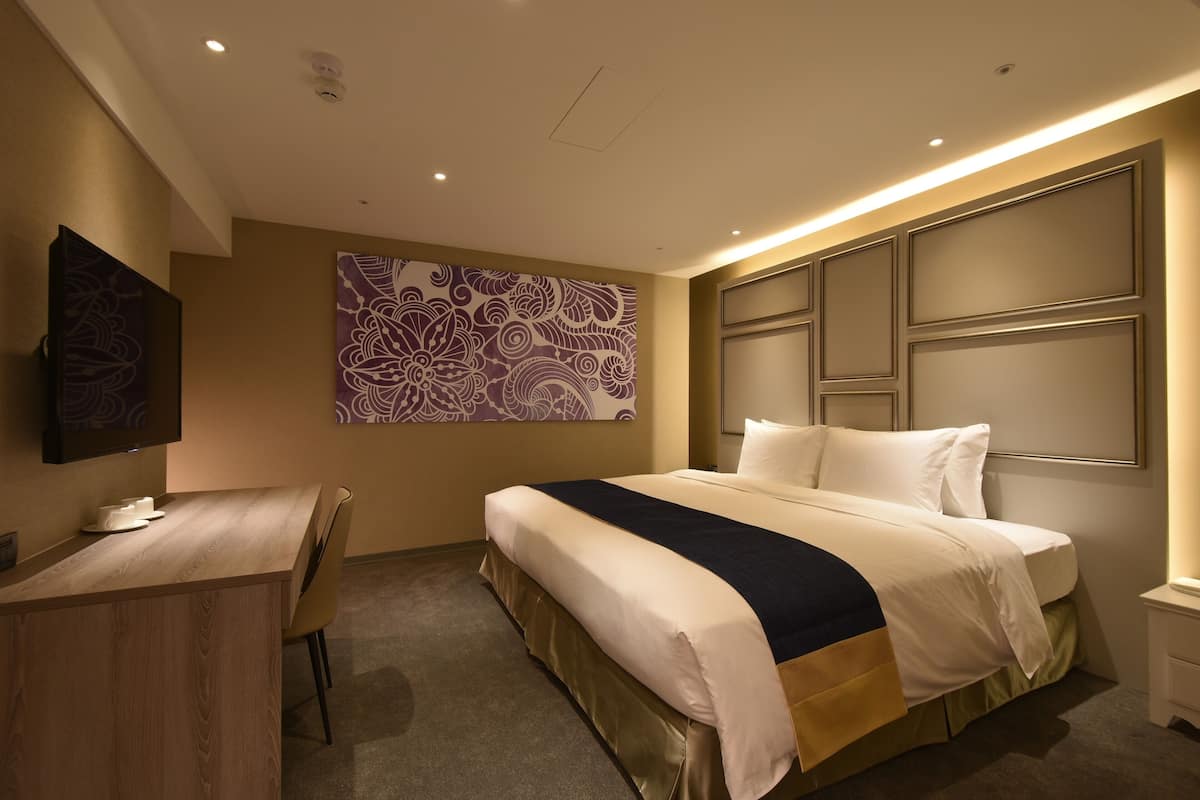 Habitación de hotel con cama, escritorio, silla, televisor y un adorno en la pared.