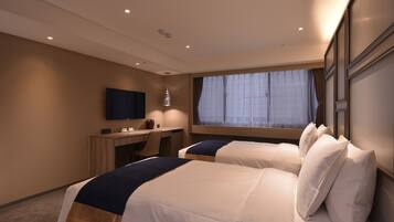 Habitación de hotel con dos camas, un escritorio, un televisor y una ventana con cortinas.