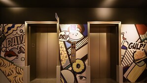 Een lift met een kleurrijke, abstracte muurschildering en een bord waarop 'DRIP' staat.