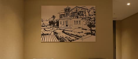 A hotel room with two armchairs, a small table, and a wall-mounted artwork depicting a house.