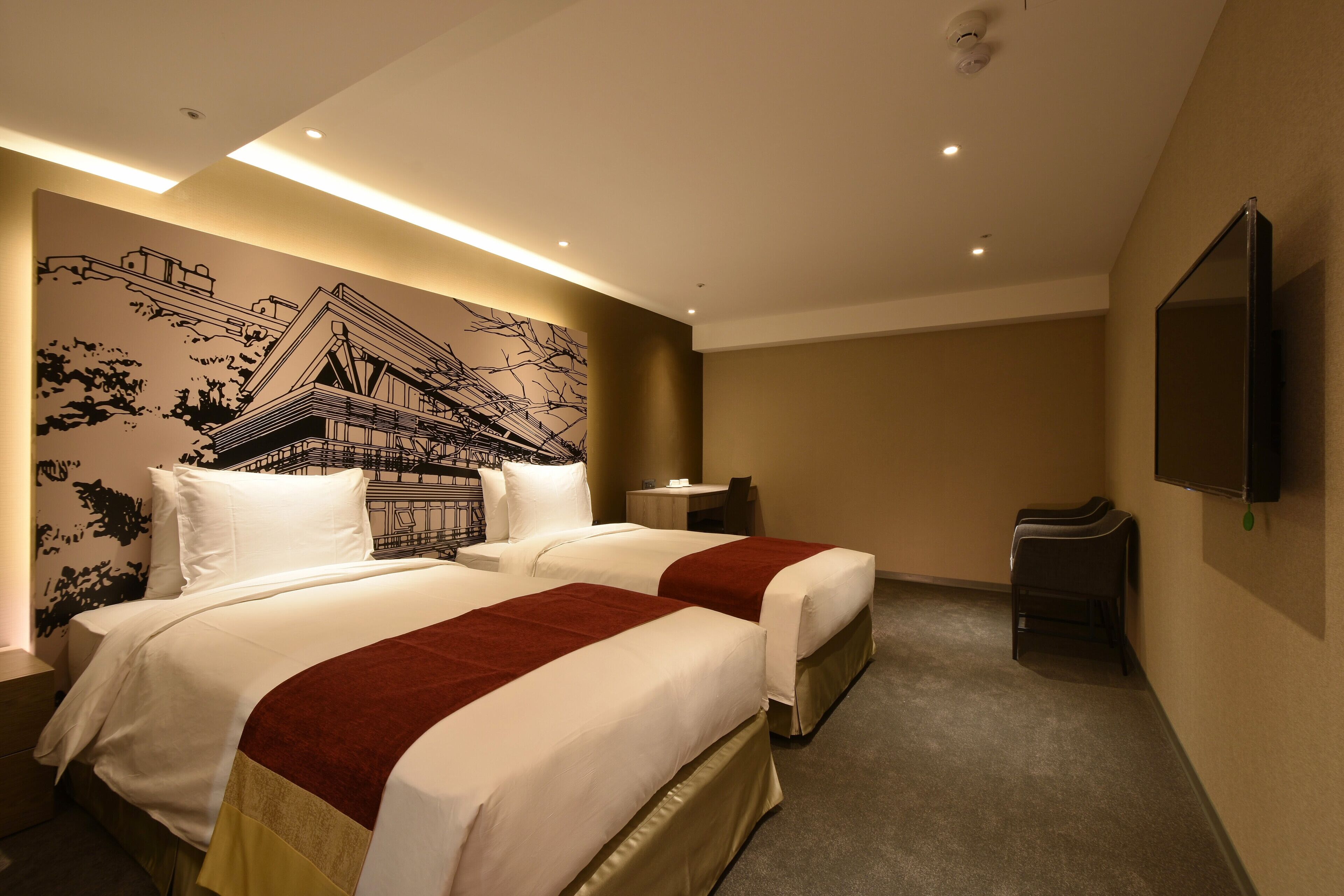 A hotel room with two beds, a wall mural, a flat-screen TV, and a small table.
