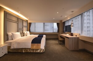 Una habitación de hotel con una cama grande, un escritorio y un ventanal con cortinas traslúcidas.