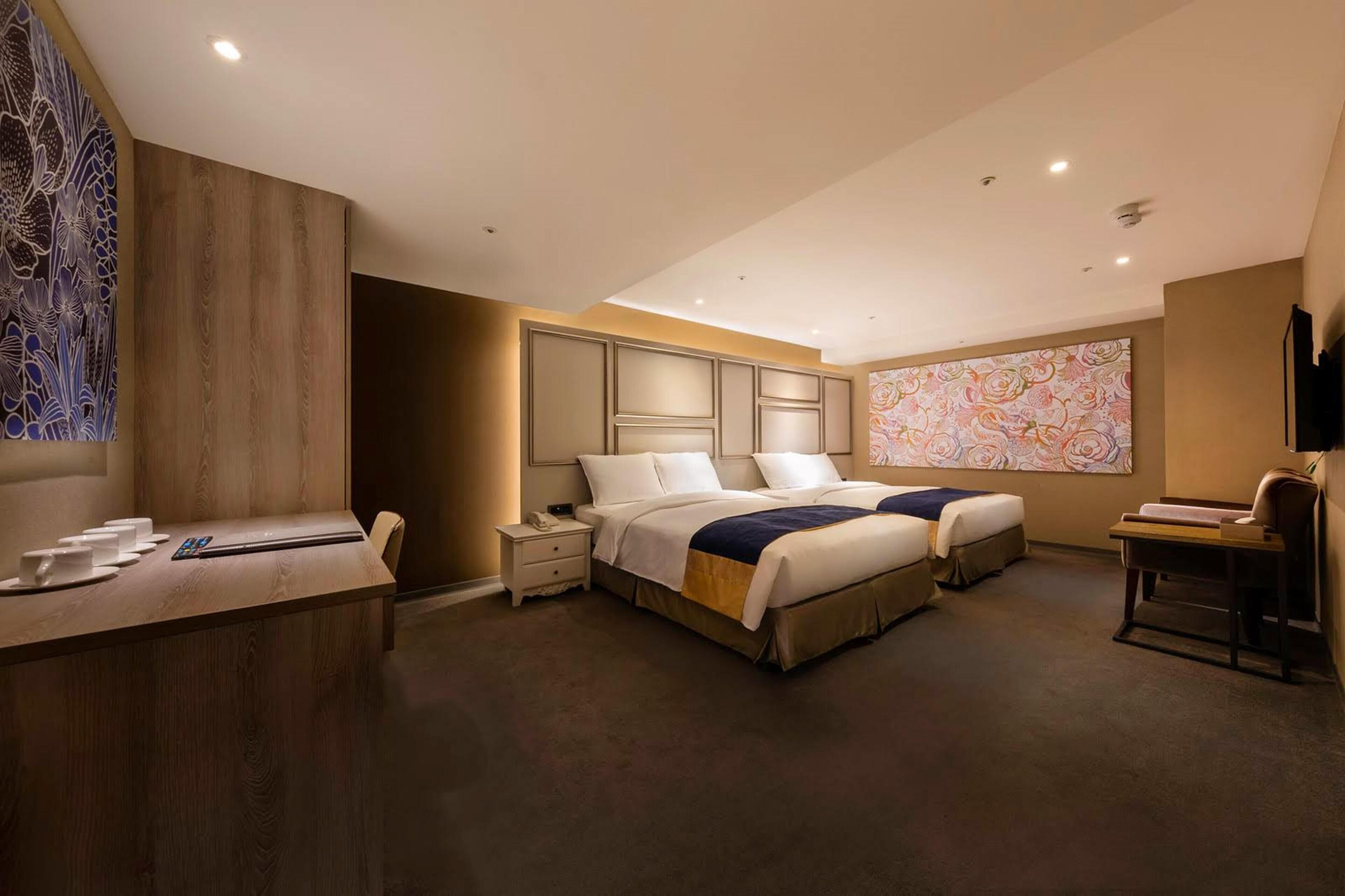 Une chambre d’hôtel avec un grand lit, un bureau avec une chaise, une petite table et un fauteuil massant.