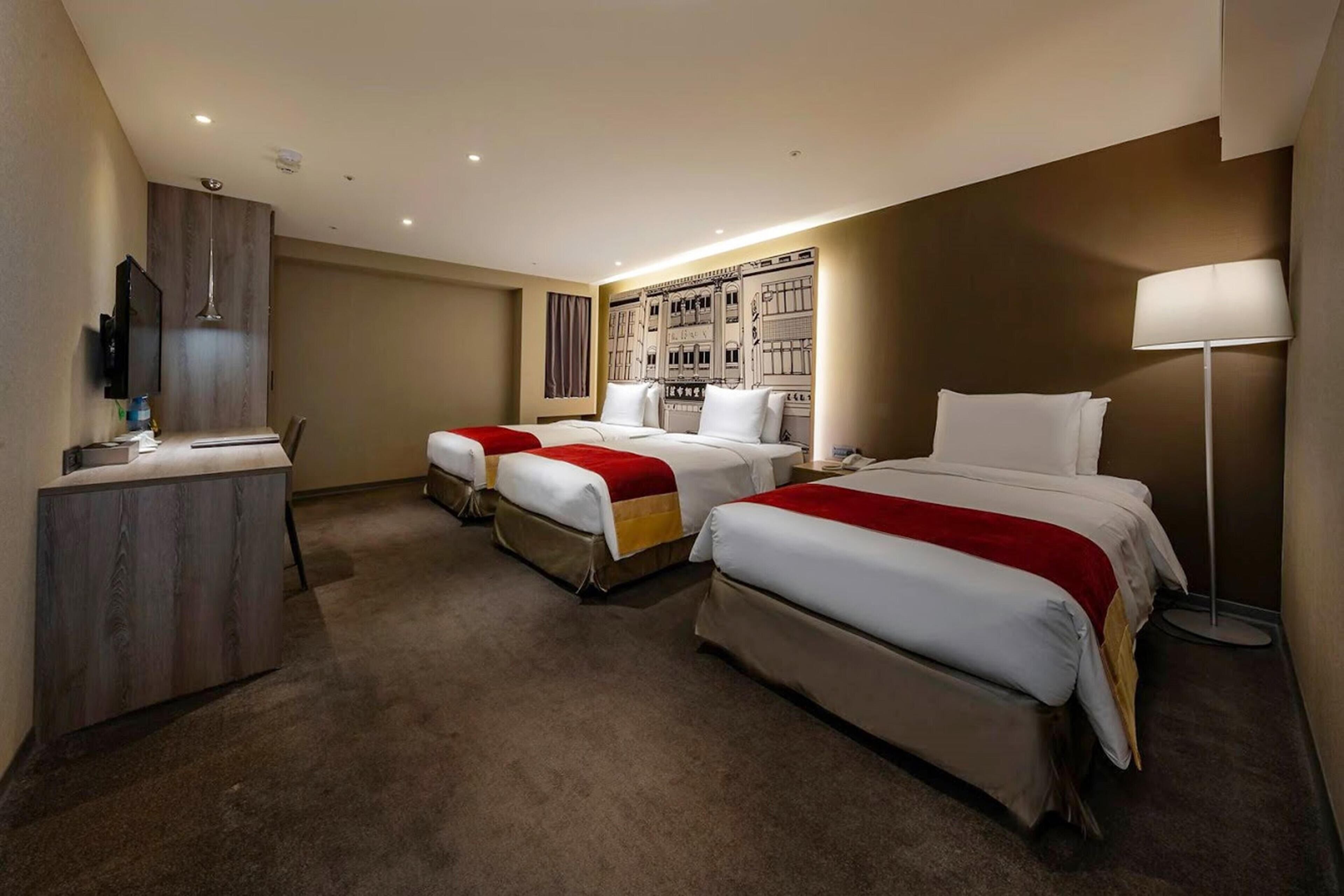A hotel room with three beds, a desk, a flat-screen TV, and a large wall mural.