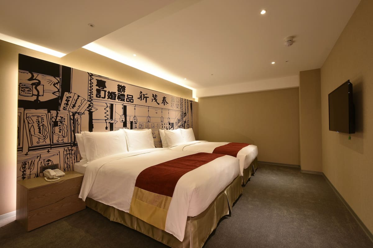 Habitación de hotel con dos camas, una mesita de noche con teléfono y una pared con un mural grande en blanco y negro.