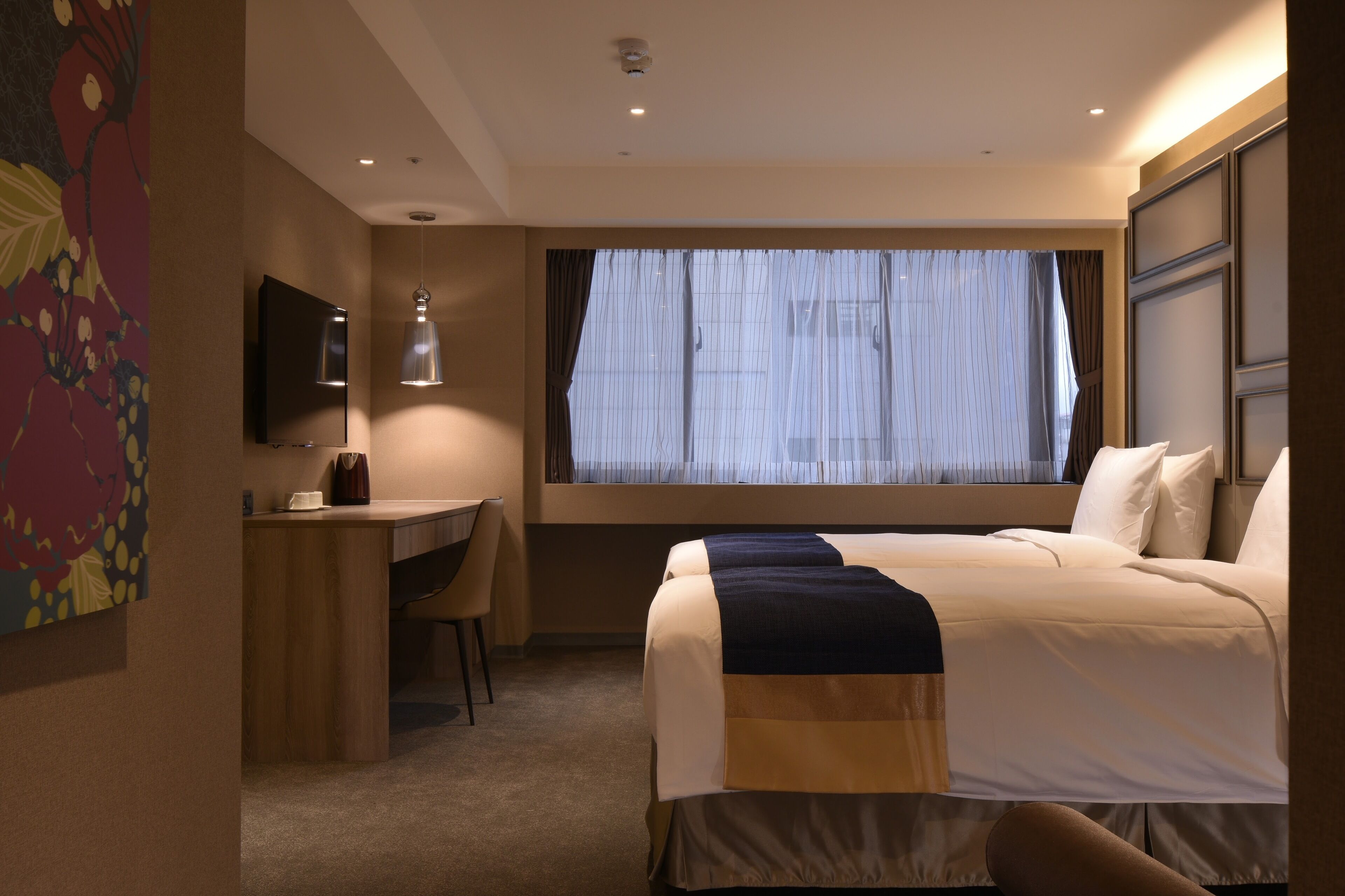 A hotel room with a bed, a desk, a chair, a TV, and a window with curtains.