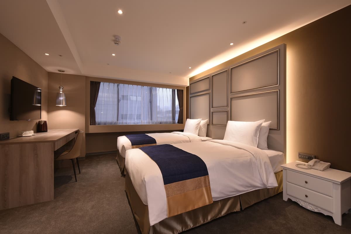 Habitación de hotel con dos camas, un escritorio, una silla, un televisor y una ventana con cortinas.