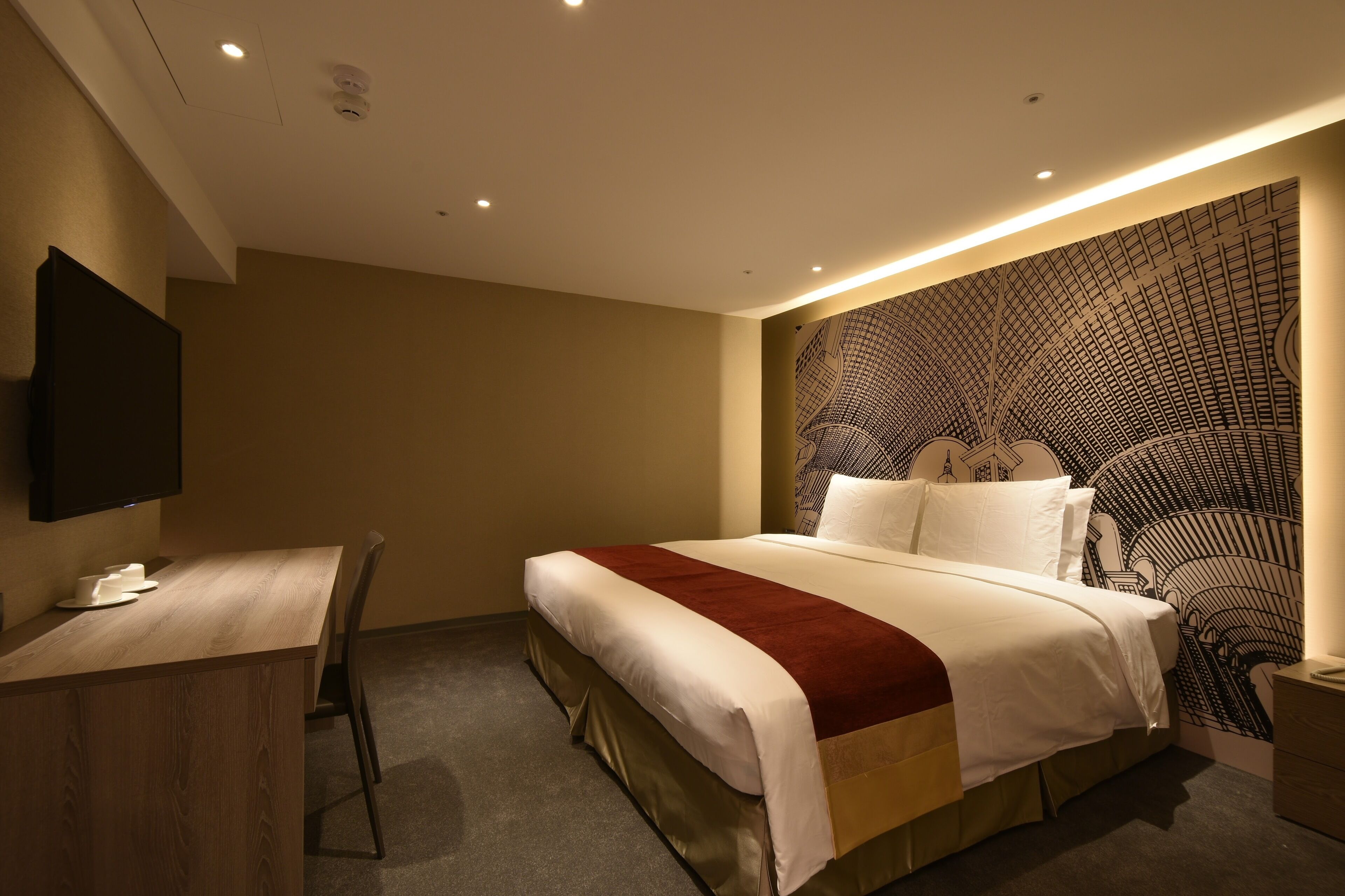 A hotel room with a bed, a desk, a chair, a TV, and a patterned wall.