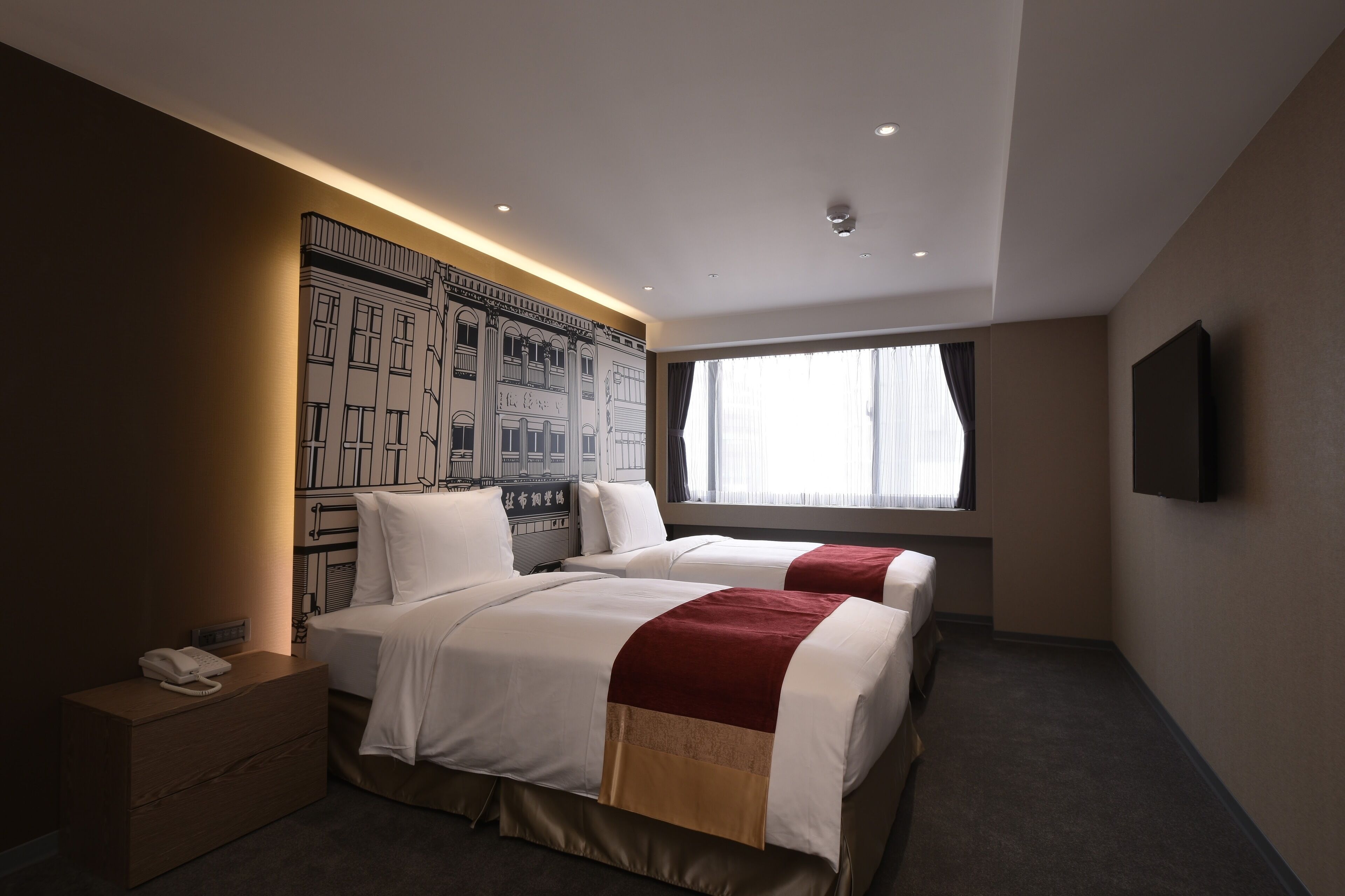 A hotel room with two beds, a large window, a mounted TV, and a wall mural.