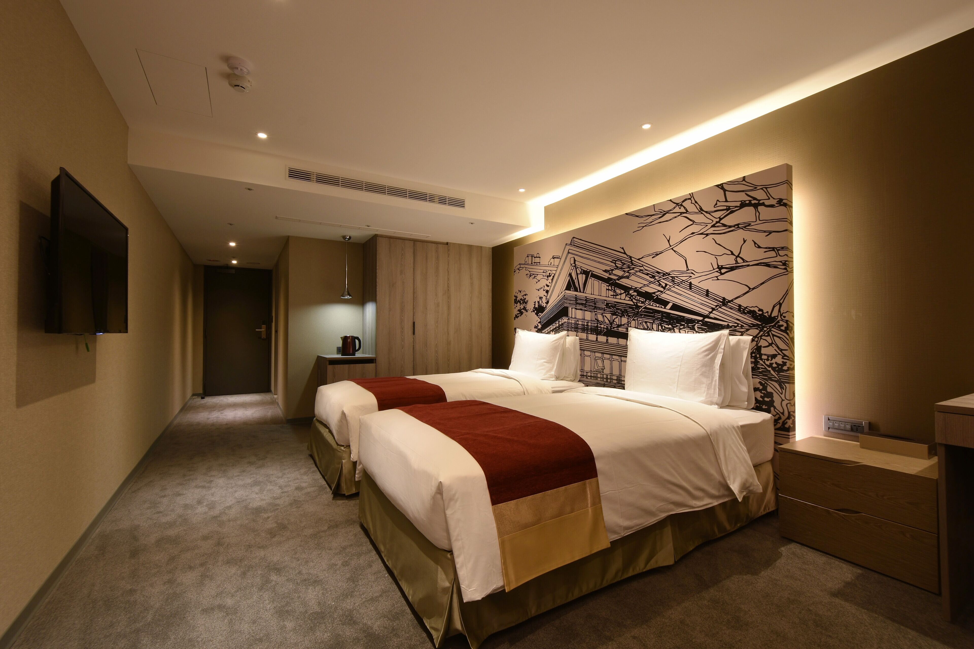 Una habitación de hotel con dos camas, un televisor de pantalla plana, una obra de arte en la pared y una mesita de noche con lámpara.