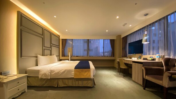 Hotelkamer met een groot bed, een bureau, een stoel, een televisie en een raam met gordijnen.