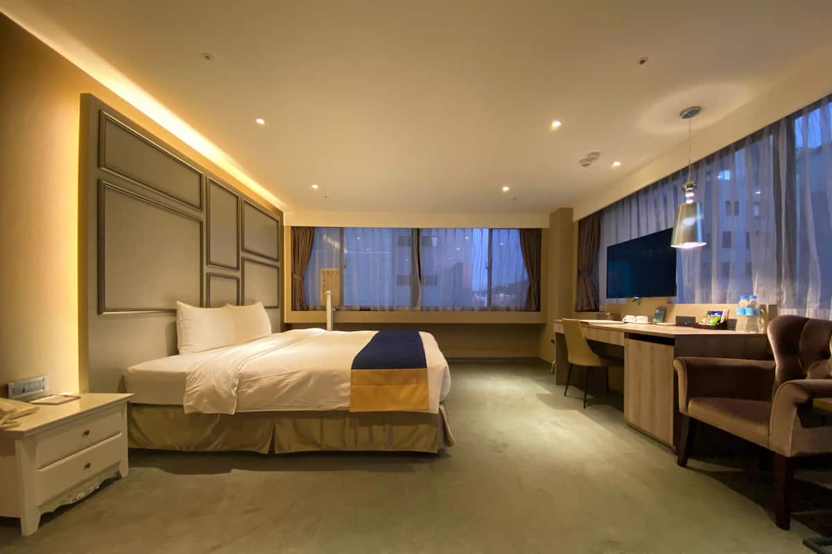 Habitación de hotel con una cama grande, un escritorio, una silla, un televisor y una ventana con cortinas.