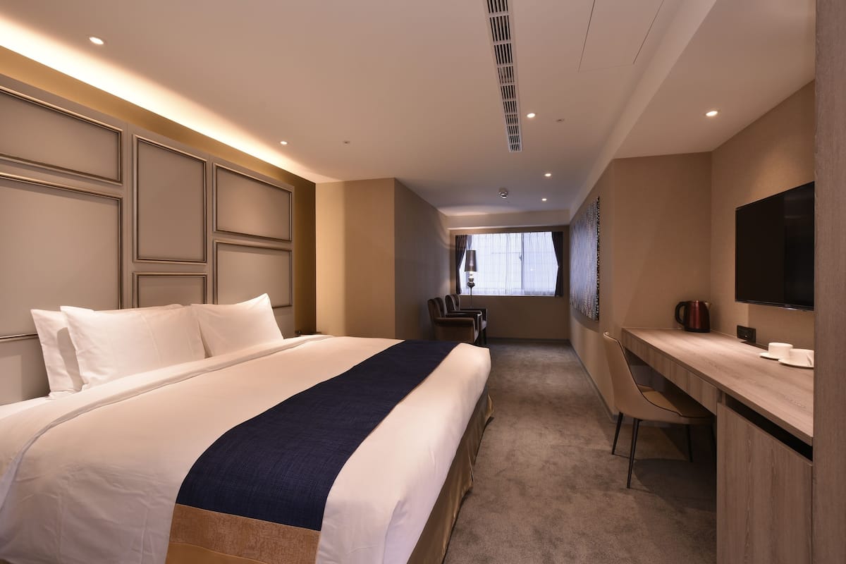 Habitación de hotel con una cama grande, un escritorio, una silla, un televisor y una ventana con cortinas.
