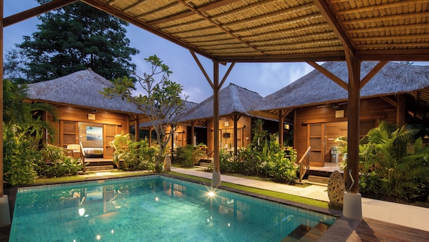 A pool area with a clear blue pool, wooden deck, and thatched-roof structures.