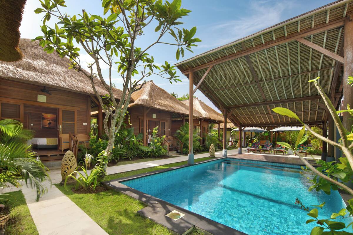A pool area with a thatched-roof structure, a covered seating area, and lush greenery.