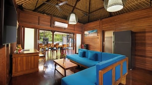 A spacious room with a wooden ceiling, a blue sofa, a wooden table, and a refrigerator.