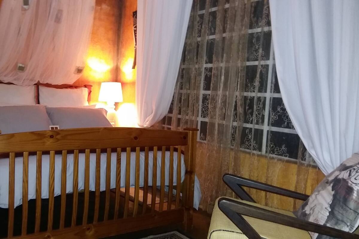 A wooden bed with a headboard, a nightstand with a lamp, and a window with curtains.