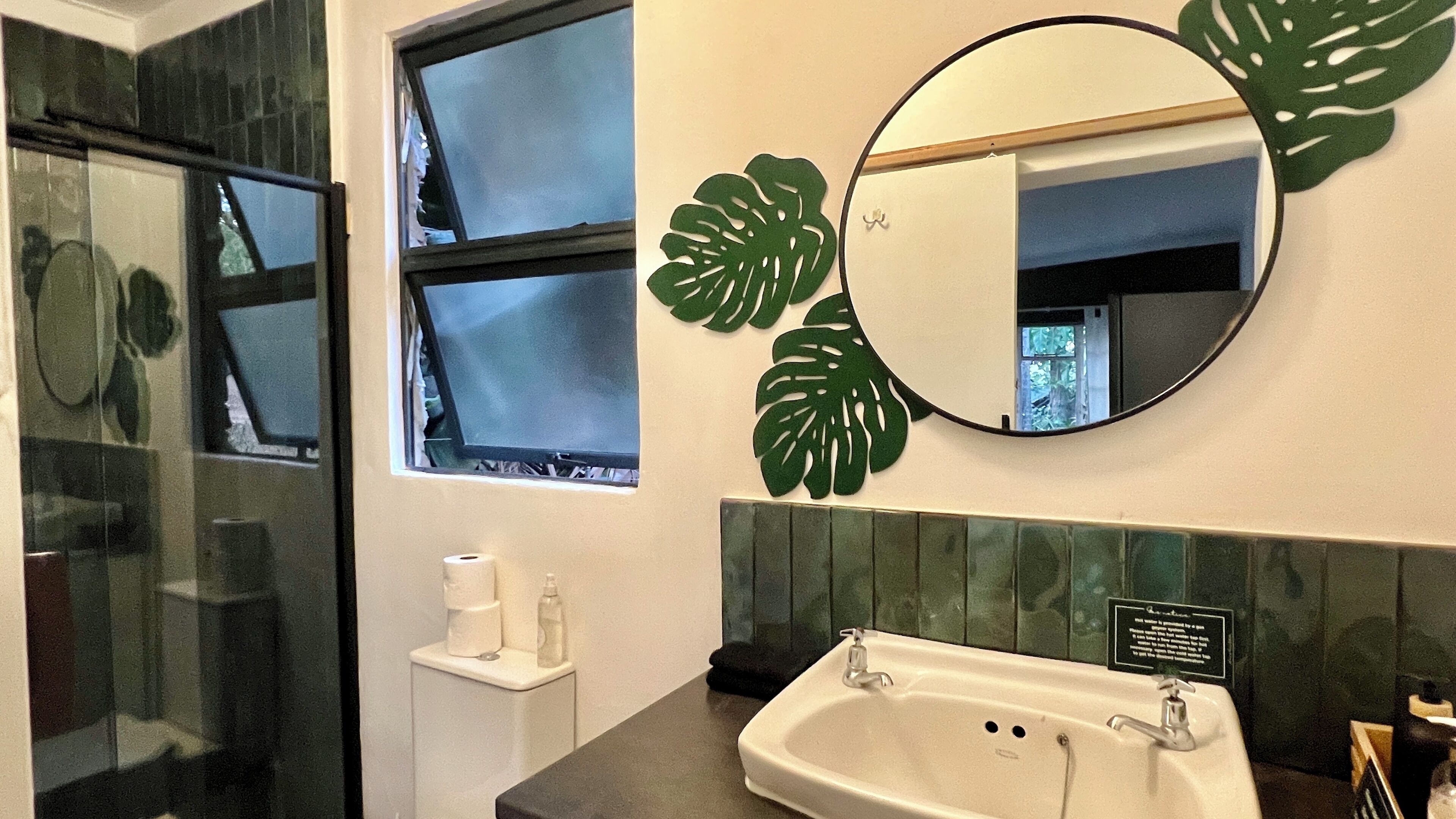 A bathroom with a sink, mirror, toilet, and windows.